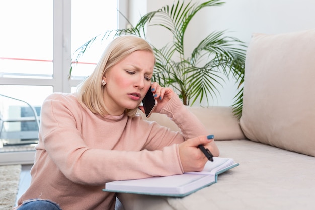 Garota trabalhando em casa, falando ao telefone e escrevendo notas em seu caderno.