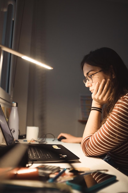 Garota trabalhando no laptop em casa ou estudante estudando em casa ou freelancer. trabalho online, trabalho de secretária à noite, escritório em casa. copie o espaço