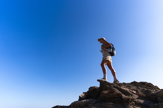 Foto garota turista com uma mochila nas costas no verão fica no topo de uma montanha