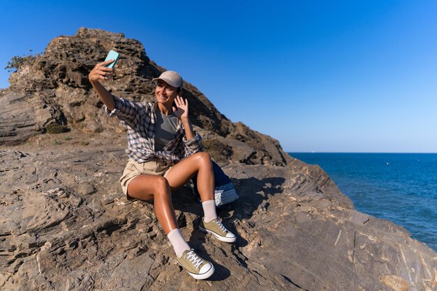 Foto garota turista com uma mochila no verão no topo de uma montanha tira uma selfie contra o fundo