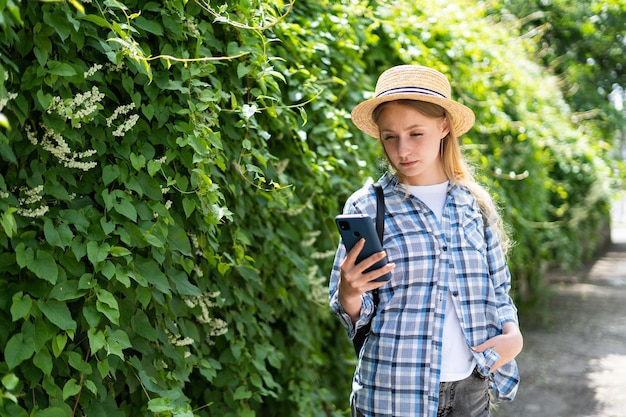 Garota turista em uma jornada grava um vídeo em um telefone celular enquanto está perto da vegetação ao fundo Uma viajante feminina está transmitindo