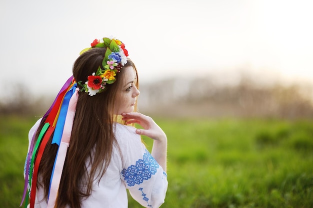 Garota ucraniana em uma camisa e uma coroa de flores na cabeça em um fundo de grama verde