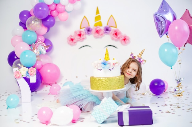 Garota unicórnio posando perto de uma ideia de bolo de feliz aniversário para decoração