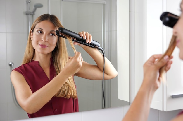 Garota usando alisador de vapor para pentear o cabelo no espelho do banheiro