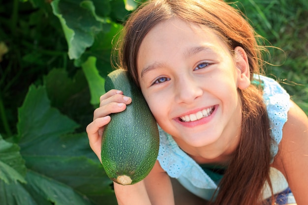 Foto garota vegana feliz com abobrinha verde fresca na horta ao ar livre