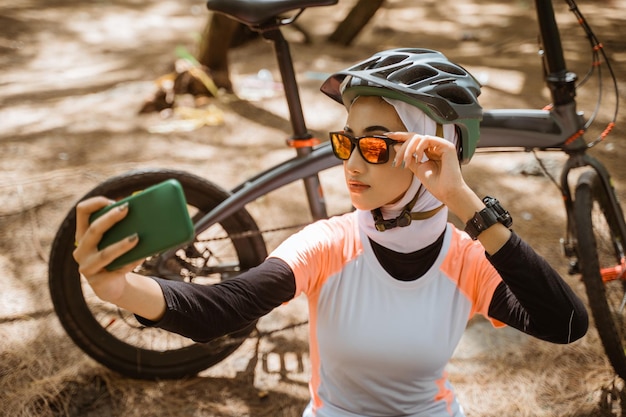 Garota velada em óculos de sol selfie usando smartphone enquanto andava de bicicleta