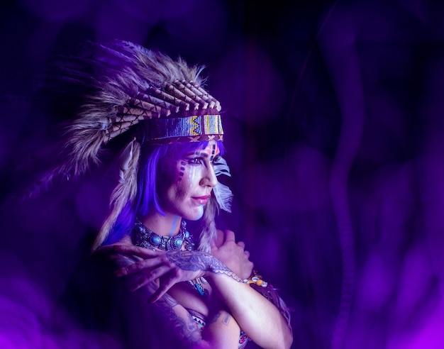 Garota vestida como um índio com penas na cabeça posa no escuro para fotografia de lightpainting.