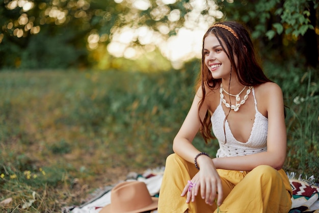 Garota vestida como uma hippie ecológica relaxando no parque sentada em um cobertor no estilo de vida descontraído do pôr do sol