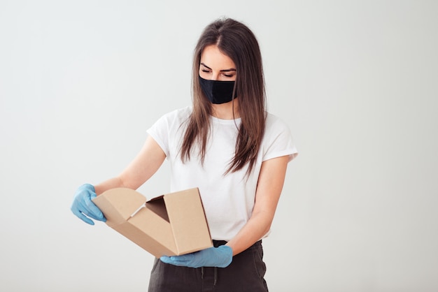 Garota vestindo máscara facial e luvas e segurando uma caixa