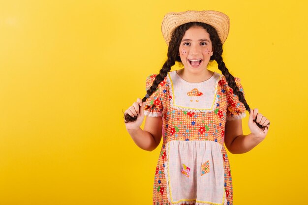 Garota vestindo roupas tradicionais de laranja para festa junina Segurando tranças de cabelo sorrindo