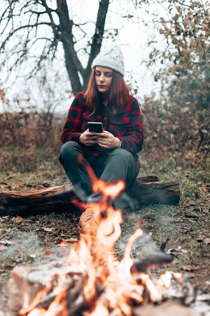 garota viajante com camisa xadrez e chapéu usa um smartphone