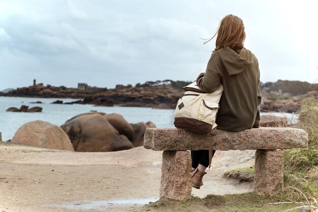 Garota viajante se senta em um banco perto do mar e da costa em Tregastel, Bretanha. França