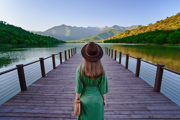 Garota viajante sozinha no cais e olhando para o lago e as montanhas. belo momento de liberdade e atmosfera serena e pacífica na natureza. vista traseira