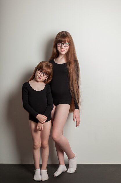 Garotas alegres em malha esportiva ficam em um tapete de ioga preto com panquecas exuberantes e cabelo saudável. irmãs felizes, retrato em um fundo branco.