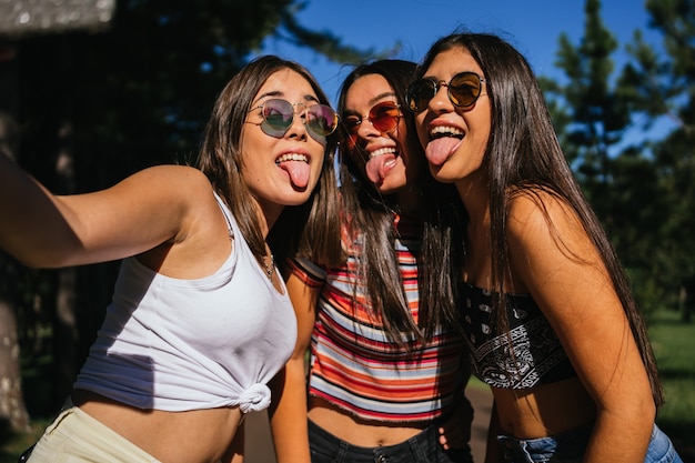 Garotas bonitas em óculos de sol brincando por aí tomando uma selfie mostrando a língua.