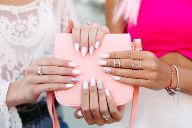 Garotas com manicure de design segurando a bolsa de couro rosa.