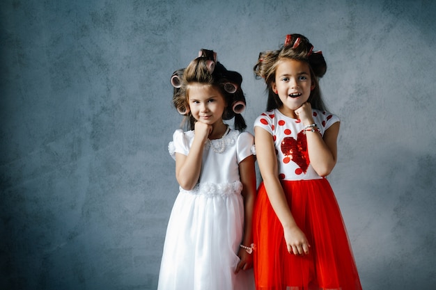 Garotas engraçadas em vestidos com rolos de cabelo posando contra a parede