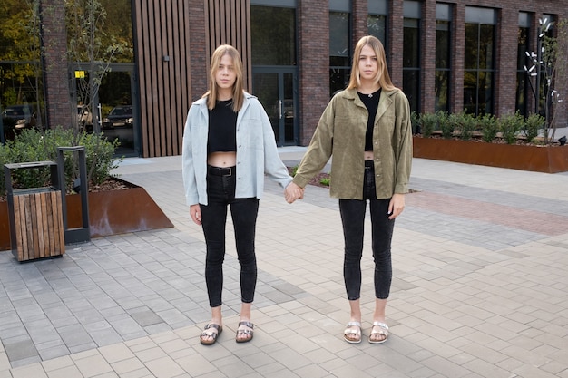 Garotas gêmeas loiras se segurando pelas mãos em um prédio moderno