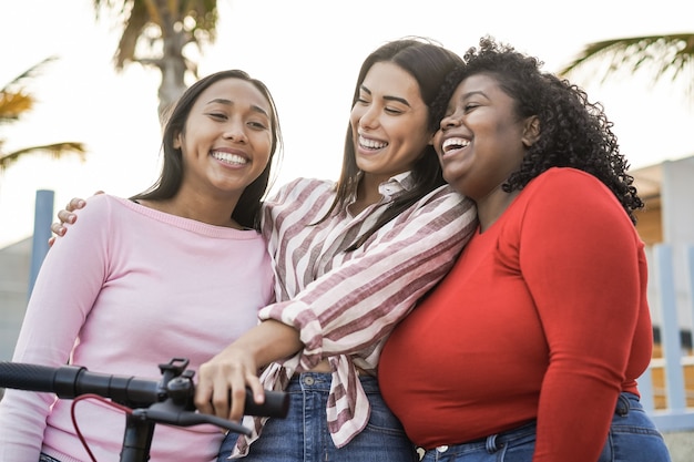Garotas latinas felizes se divertindo com uma scooter elétrica ao ar livre na cidade - foco principal no olho da mulher africana