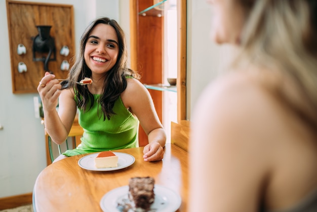 Garotas latinas sentadas em um café comendo bolos e ouvindo a história de vida engraçada de uma amiga