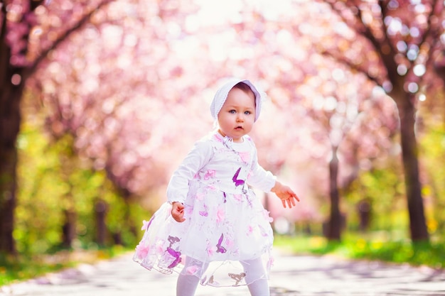 Foto garotinha adorável andando sob a cerejeira florescendo com flores cor de rosa em um lindo jardim de primavera