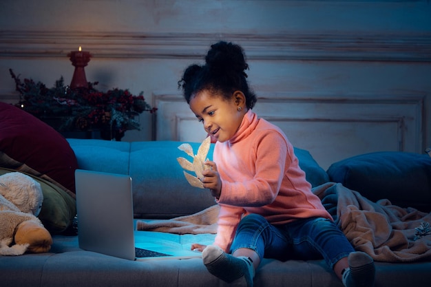 Garotinha afro-americana feliz durante uma videochamada com laptop e dispositivos domésticos