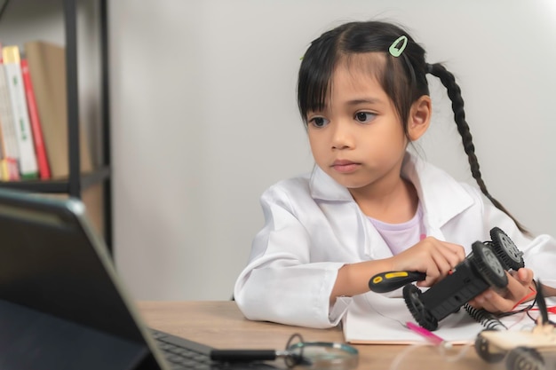 Garotinha asiática construindo e codificando robôs na classe STEM Consertando e consertando carros mecânicos de brinquedo