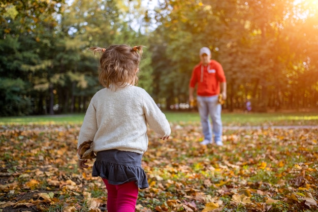 garotinha brinca com o pai ao ar livre no parque outono.