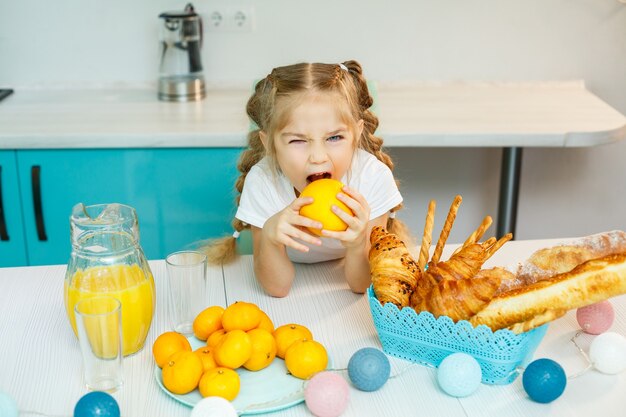 Garotinha brincalhona e divertida, feliz, segurando laranjas, com a cozinha ao fundo