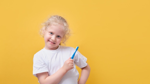 Garotinha de 6 anos segurando a escova de dentes na mão, escovando o fundo amarelo do dente