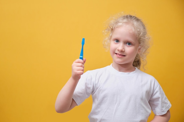 Garotinha de 6 anos segurando a escova de dentes na mão, escovando o fundo amarelo do dente
