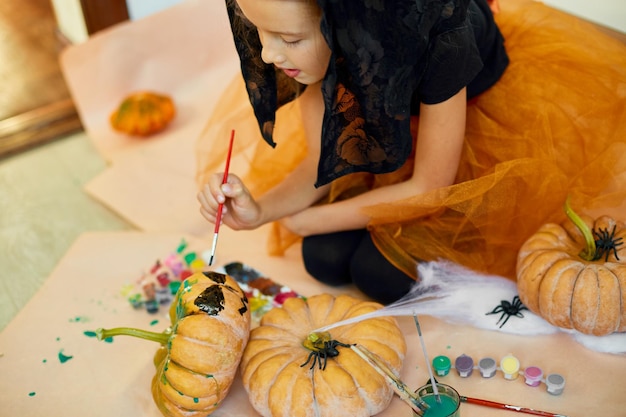 Garotinha desenhando rosto na abóbora laranja de halloween jackolantern