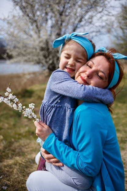 Garotinha e mãe mulher caminham pela floresta de primavera com árvores floridas, riem e brincam, o início da primavera, férias em família, amor dos pais