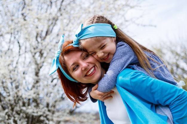 Garotinha e mãe mulher caminham pela floresta de primavera com árvores floridas, riem e brincam, o início da primavera, férias em família, amor dos pais