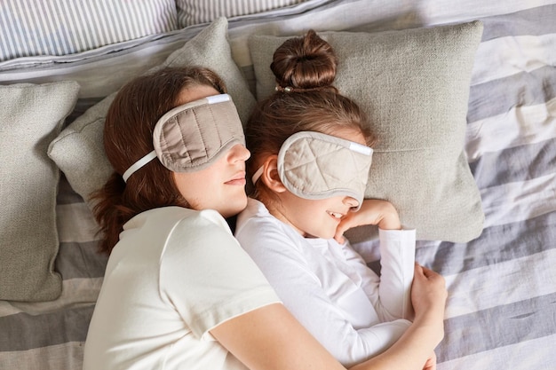 Garotinha e sua mãe aproveitando a manhã dormindo juntas abraçando-se com os olhos vendados tendo o dia cochilando juntas no quarto fim de semana preguiçoso