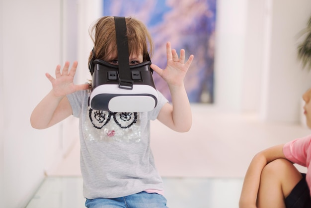 Foto garotinha em casa usando óculos vr colocando as mãos para cima e jogando