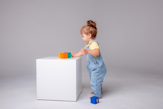 Garotinha em um fundo branco e brincando com cubos coloridos. brinquedo infantil cu