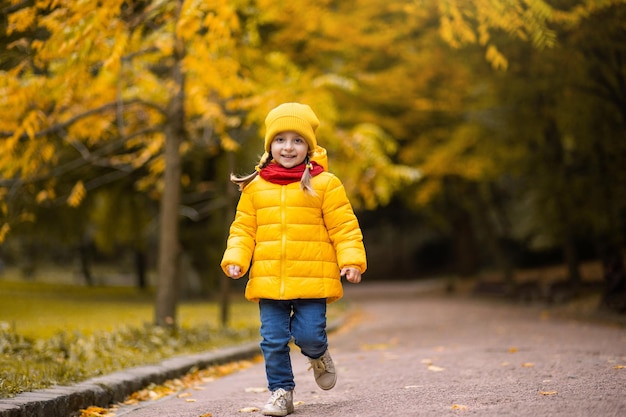 Garotinha engraçada corre e sorri em fundo de árvores amarelas no parque outono. criança em uma caminhada no parque outono. menina pré-escolar correndo e rindo no beco do parque.