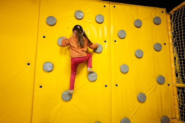 Garotinha escalando a parede no parque infantil amarelo Criança em movimento durante entretenimentos ativos