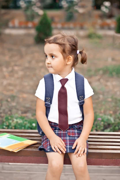 Garotinha fofa de uniforme, sentada em um banco e rindo