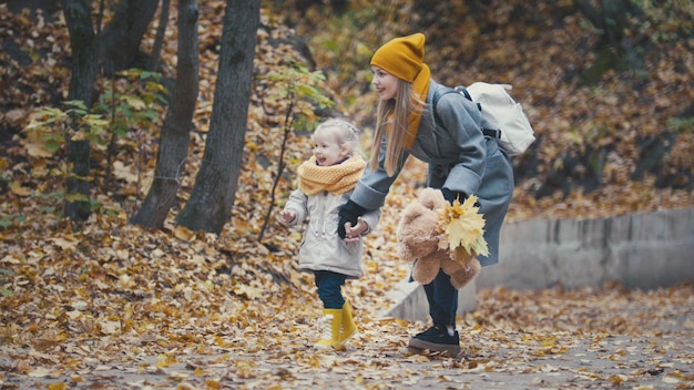 Garotinha loira com a mãe coletando folhas no parque do outono, close-up