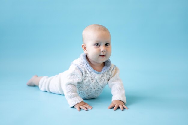 Garotinha loira com um suéter de malha em um fundo azul isolado, espaço para texto, bebê pequeno em roupas de inverno, inverno