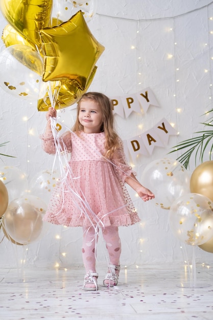 Garotinha loira feliz de vestido rosa segurando balões e comemorando seu aniversário