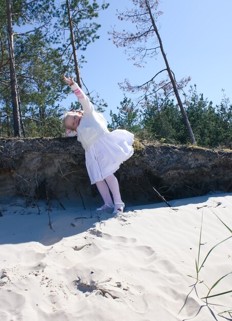 Garotinha loira feliz em um vestido branco caminha na praia na costa do mar báltico.