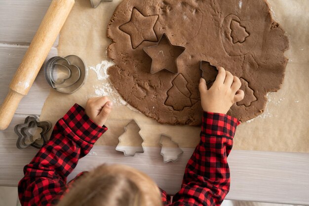 Garotinha menina de pijama vermelho cozinhando pão de mel festivo no natal decorado cozinha natal c ...