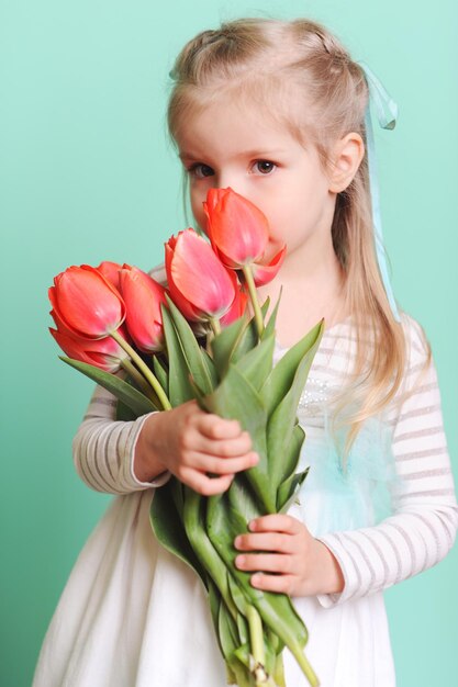 Garotinha segurando tulipas vermelhas usando vestido elegante olhando para a câmera