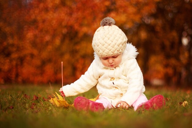 garotinha sentada nas folhas caídas no parque de outono