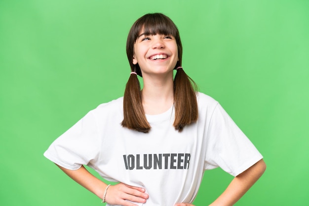 Garotinha voluntária sobre fundo isolado posando com os braços no quadril e sorrindo