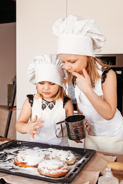 Garotinhas provam açúcar na cozinha usando chapéus brancos de chef