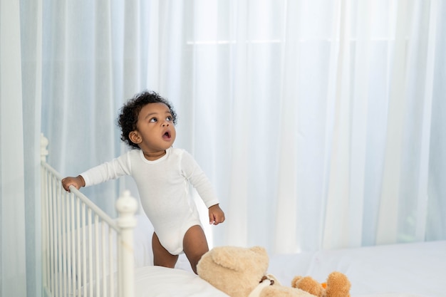 Garotinho afro-americano feliz subindo na cabeceira da cama e procurando algo para aprender